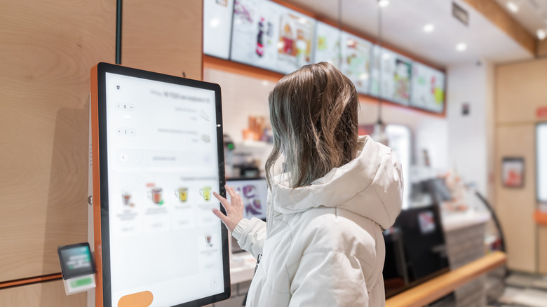 A young woman interacts with a digital kiosk in a stylish caf, selecting items for her order.