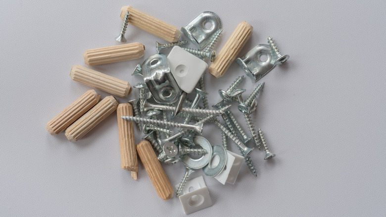 Various metal screws, nuts and bolts, wooden dowels and joints used for assembling furniture laid out on plain grey background to portray a DIY concept.
