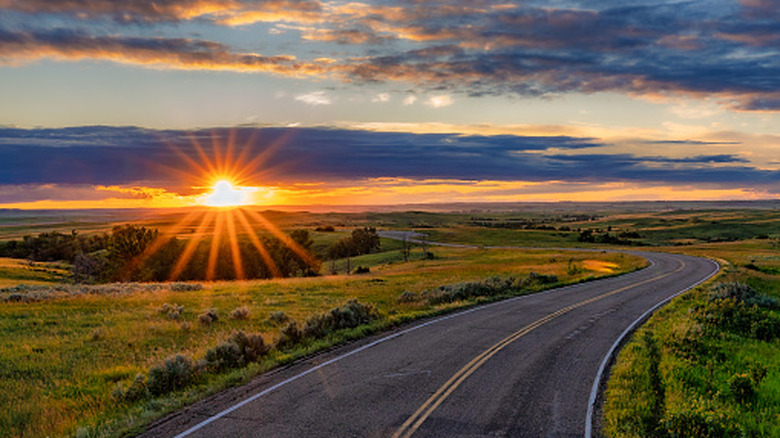 Sunrise over a grassy plain with a winding road through it.