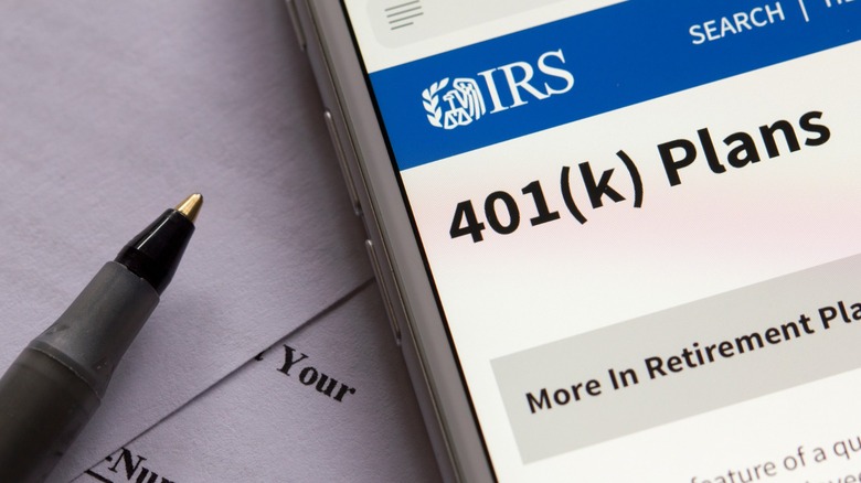 Close-up of a smartphone displaying an IRS webpage about 401(k) plans next to a pen and printed documents