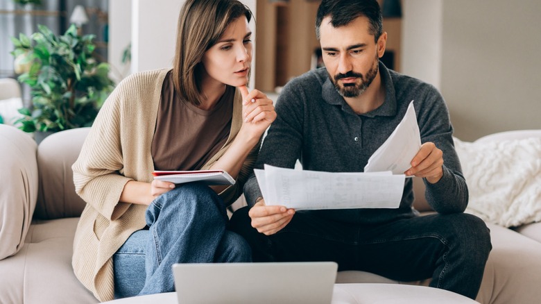 A couple sitting on a couch reviewing paperwork together, with a laptop in front of them