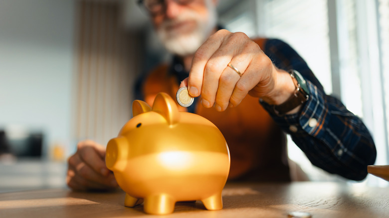 Senior adding money to piggy bank.