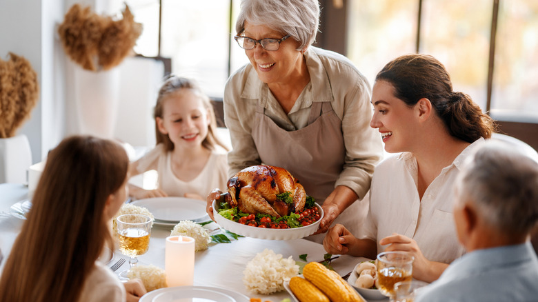 woman bringing a turkey to the table with family