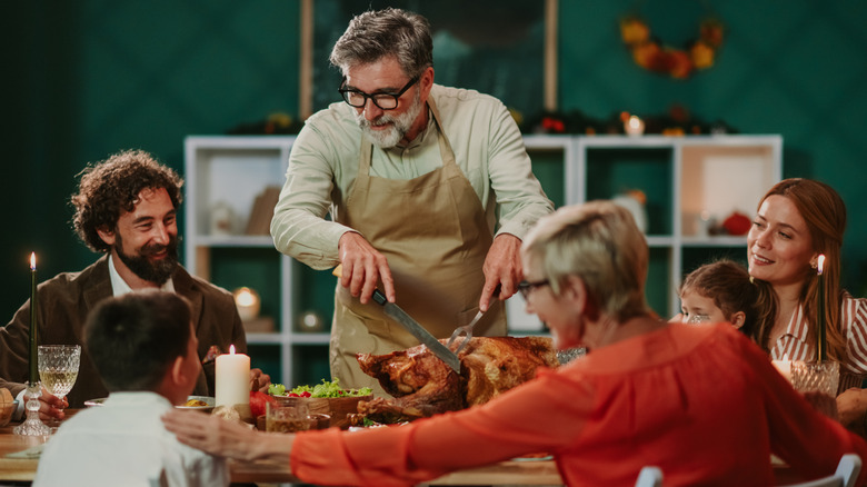 Man carving turkey at a dinner table with friends