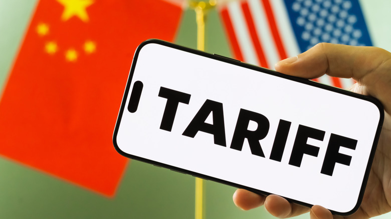 Person holding smartphone displaying the word TARIFF in bold letters, with the national flags of China and the United States in the background