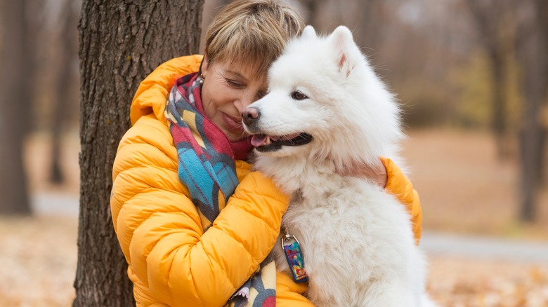 woman in yellow jacket hugging white dog