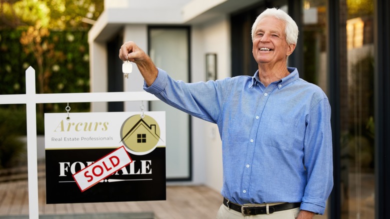 mature man standing with sold house sign