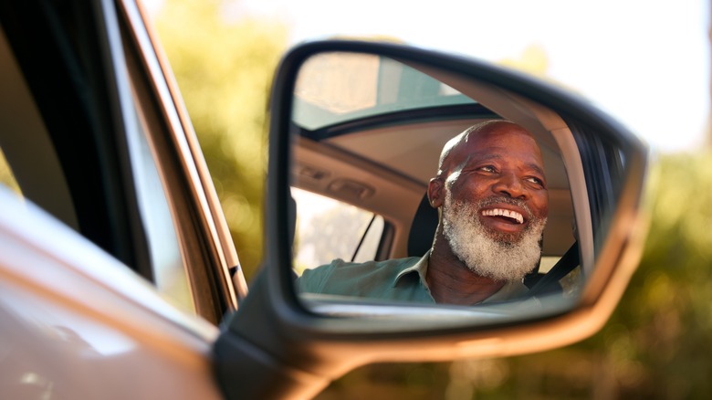 smiling mature man reflected in car mirror