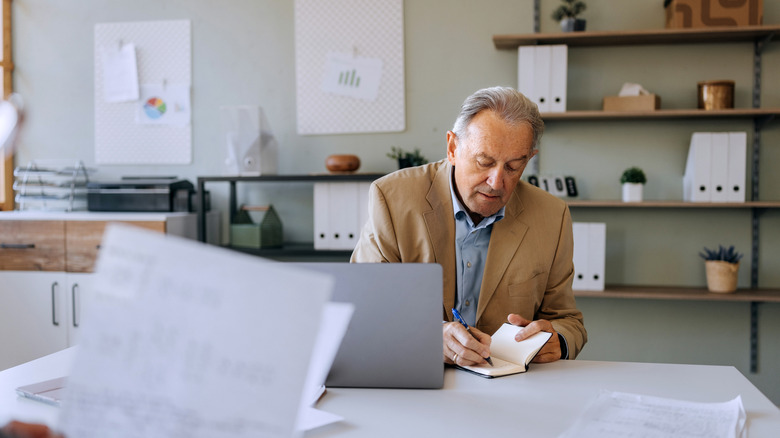 man looking at laptop and writing in notebook