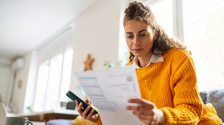 While organizing home finances, woman using mobile phone to calculate.