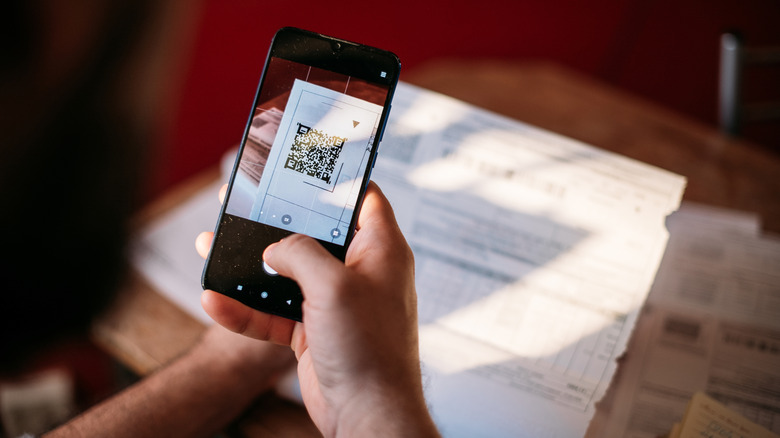 A man pays utility bills online using a QR code in an app using a smartphone in the kitchen.