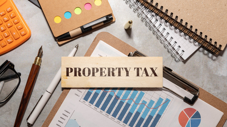 A wooden board with the words Property Tax written in caps and an assortment of office supplies on a desk.
