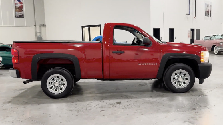 A red 2007 Chevrolet Silverado 1500 parked in a large white garage with classic cars parked behind it