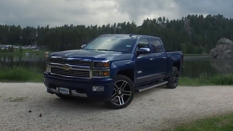 A dark blue 2015 Chevrolet Silverado parked on a rural street with a lake and trees in the background