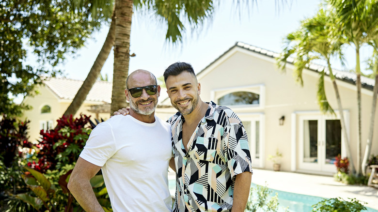 Two smiling men hugging in their backyard in front of a pool.