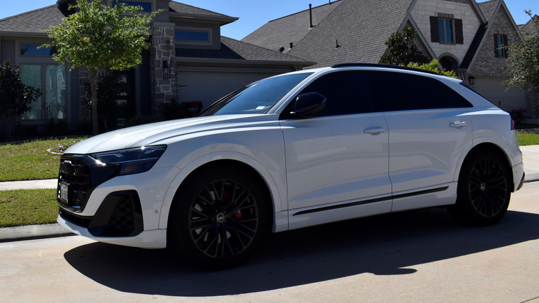 A luxurious white Audi RS Q8 luxury car parked in front of luxurious homes