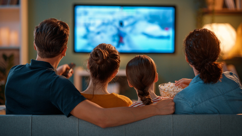 Shot of a family of four from behind as they sit on a couch watching TV