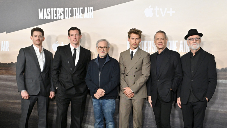 Group of six men stand in front of a board that features the words Masters of the Air