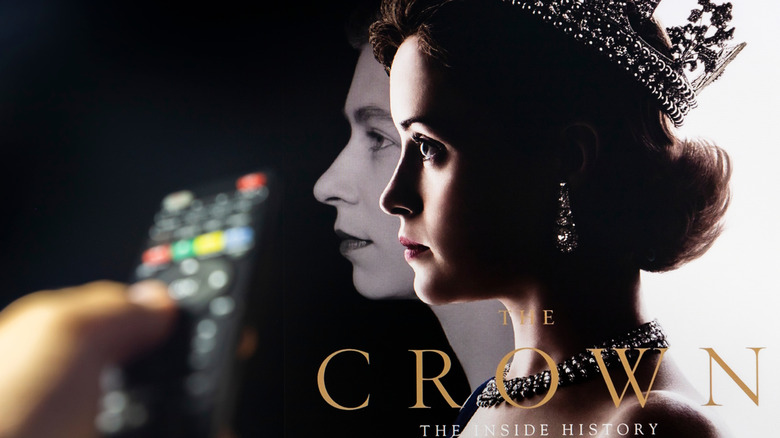 Hand holds remote pointed at TV with image of The Crown on screen