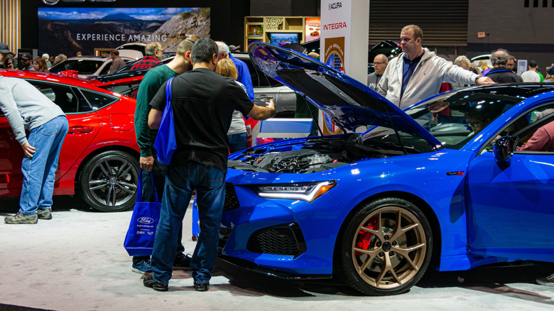 People looking under the hood of an Acura TLX at a car show.