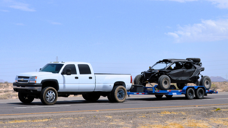 A Chevrolet Siverado towing a dune buggy on a desert road.
