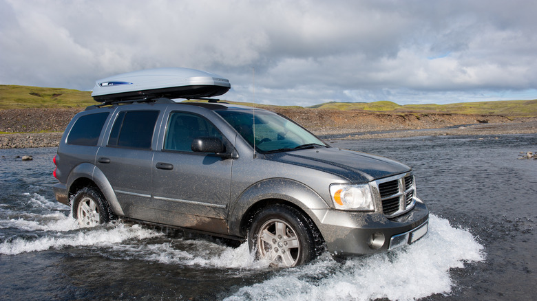 A Dodge Durango driving across a stream of water in grassy area.