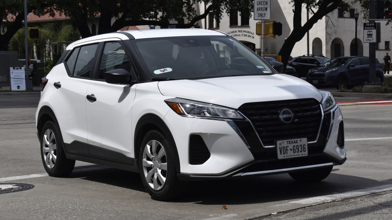 A portrait of a white Nissan Kicks SUV cruising in a downtown district