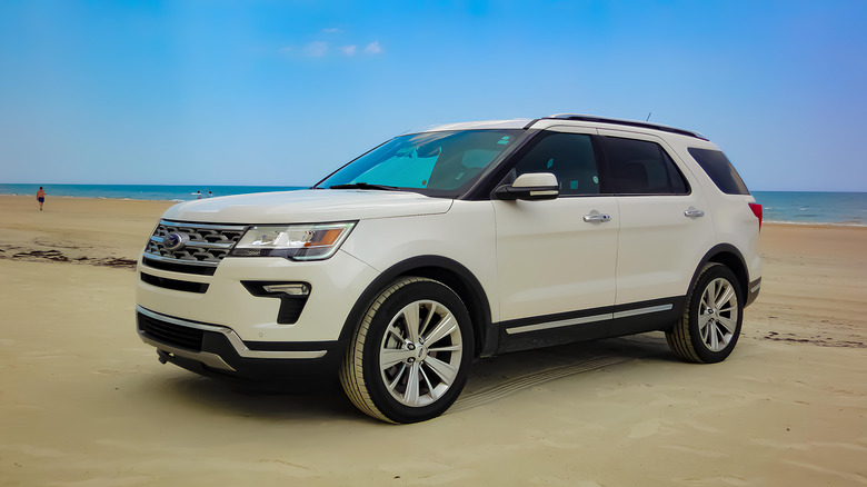 A white Ford Explorer parked on the sand at Daytona Beach during a sunny afternoon.