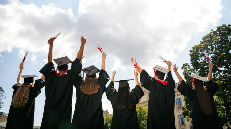 Graduating students in caps and gowns holding diplomas with their arms in the air