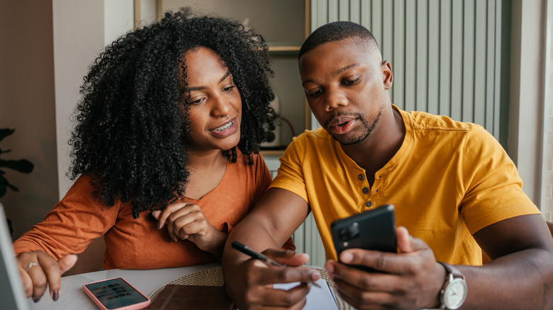 A young couple weighing their investment options using their phones and a laptop
