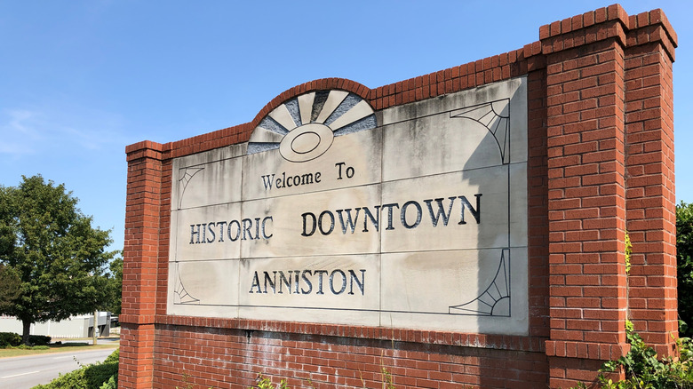 The photograph captures the welcoming sign for the city of Anniston, Alabama, standing proudly against a vibrant blue sky.