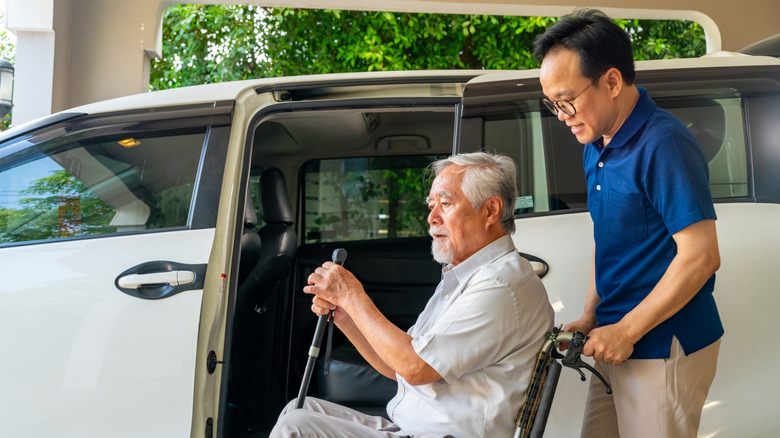 A senior man in a wheelchair being assisted into a transport vehicle.