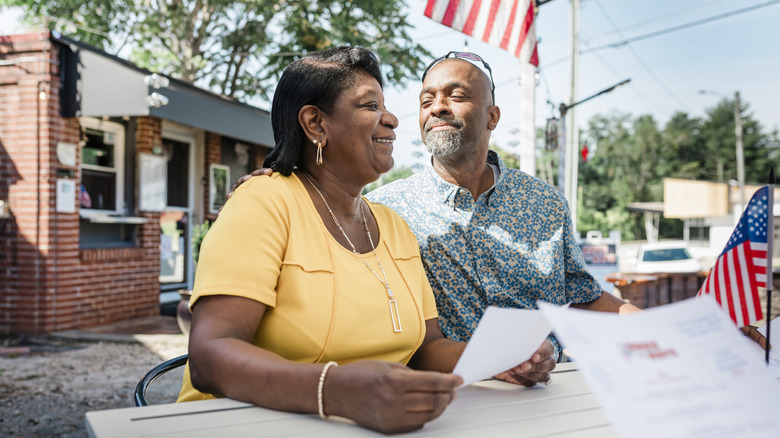 A smiling mature couple sitting on a patio with a tiny American flag.