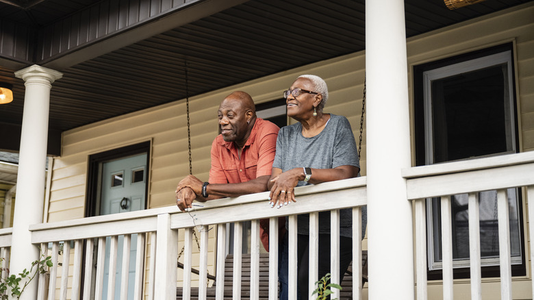 A mature couple standing on their front porch watching the world go buy.