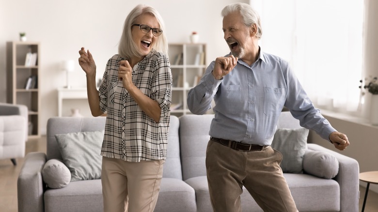 A jubilant mature couple dancing in their living room.