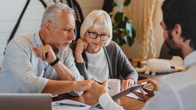 A mature couple signing an insurance policy in an insurance broker's office.
