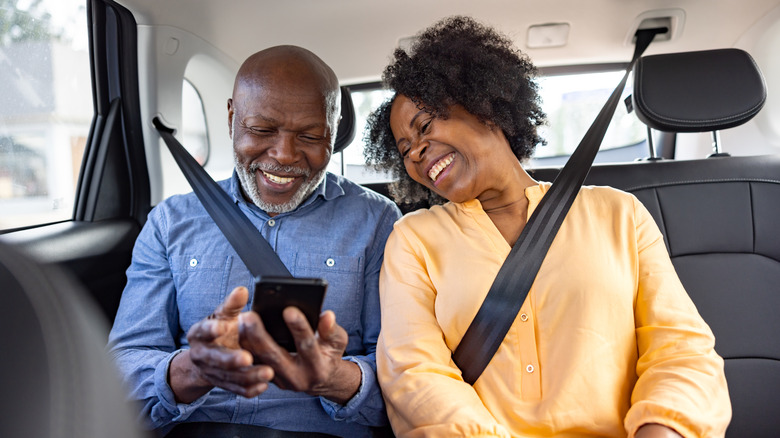A happy mature couple in the backseat of an uber looking at a phone.