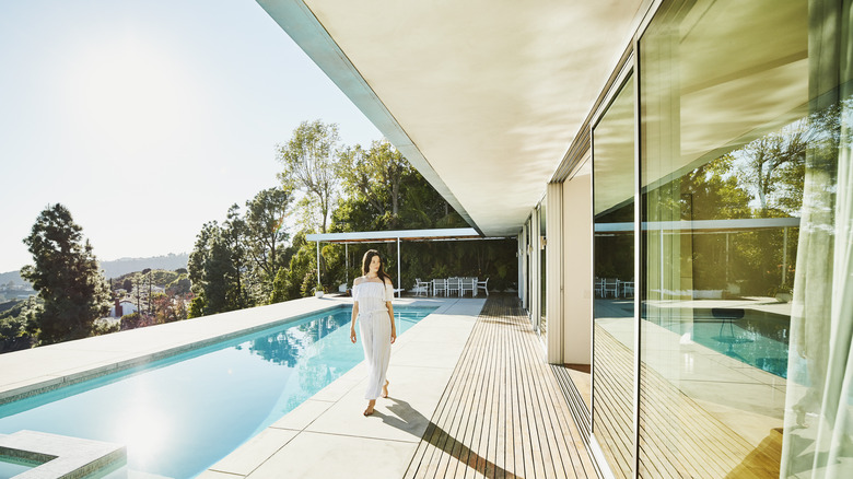 A woman walking beside an infinity pool outside of a mansion in California.