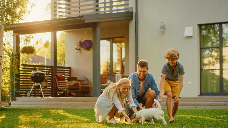 A happy family in the backyard of a huge home playing with a puppy.