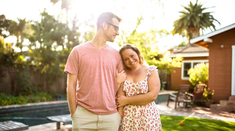 A happy couple in an embrace in a backyard with a sunlit pool in the background.