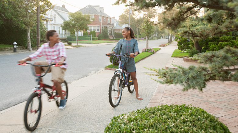 Two smiling kids bike riding down an idyllic New York suburb.