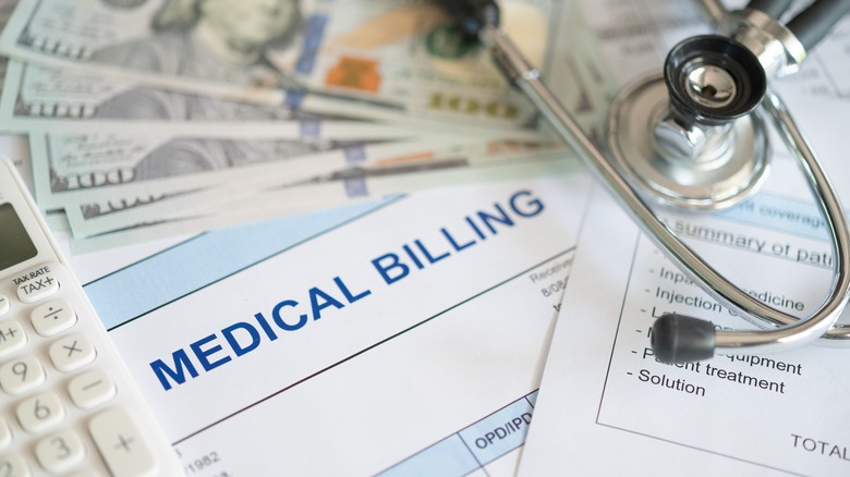 Medical billing document and dollar banknote, calculator, and stethoscope.