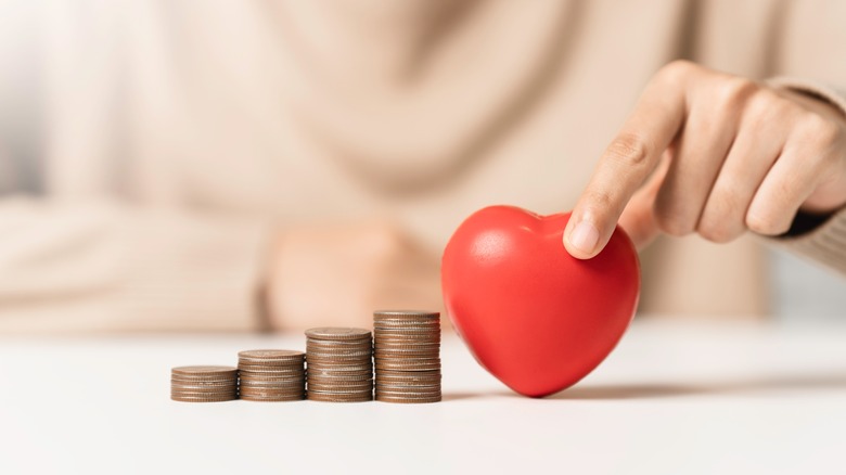 Woman holding red heart shape and money coin stack.