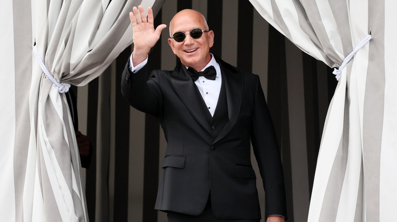 A smiling Jeff Bezos waving in a tuxedo.