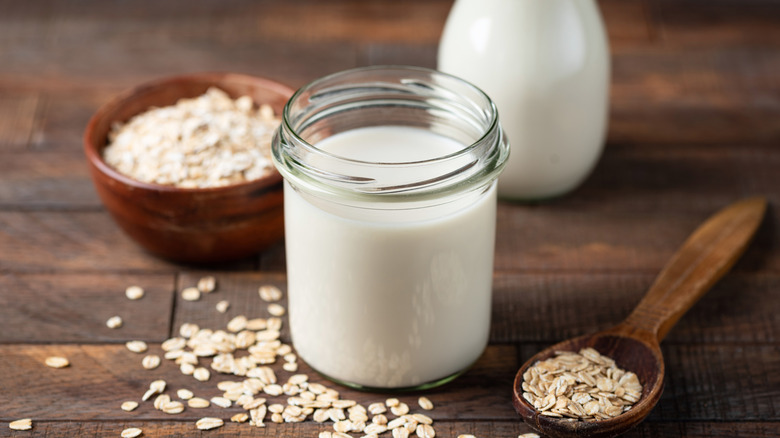 Oat milk in glass jar on wooden table.