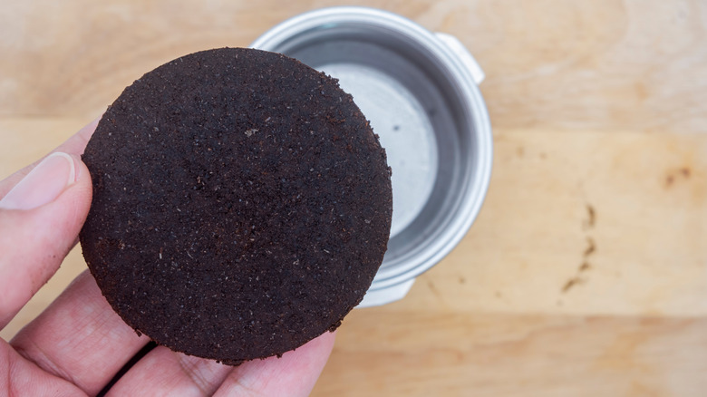 Hand holding an extracted espresso coffee puck over the portafilter.