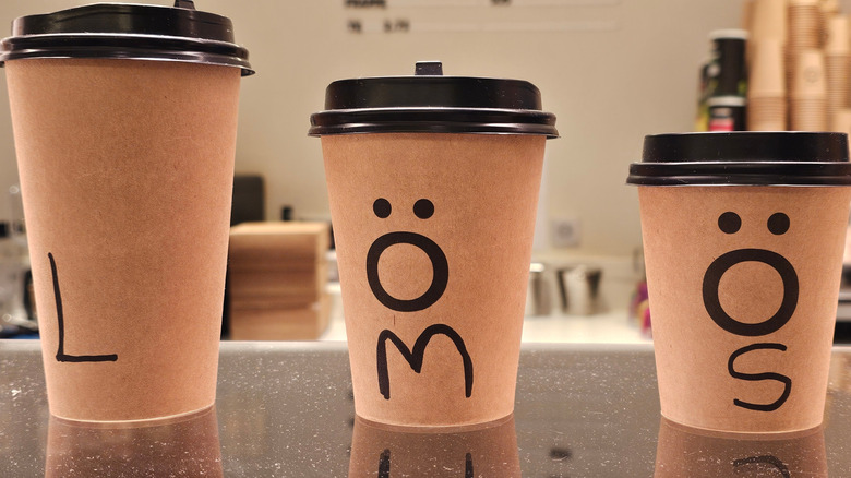 Three takeaway coffee cups of different sizes on a café counter.