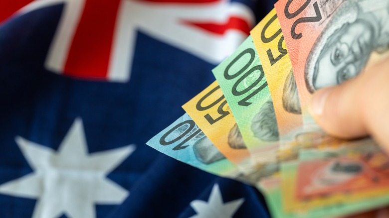 New Australian dollars held in hand against the Australian flag.