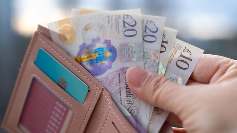 Female hand taking out multiple British Pound banknotes out of a wallet.