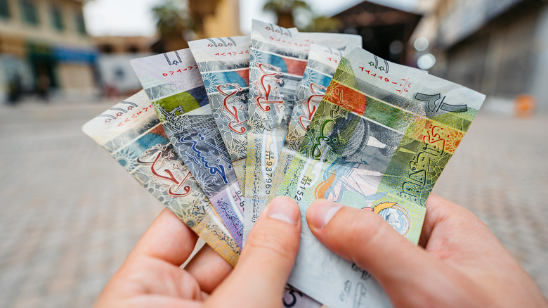 Young man holding Kuwaiti dinar on the street in Kuwait City in Kuwait.